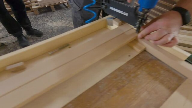 Craftsman in a carpentry workshop hammers nails with a pneumatic hammer. Making a stool