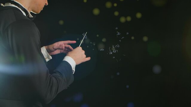 In a close up shot, a man in a tuxedo stands against a black background. He is a conductor and conducts with a baton. Multi-colored notes and a treble clef float around him. Demonstrates musical art