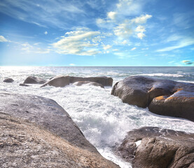 Copy space ocean view of beach with foamy sea water crashing onto boulders and rocks on a peaceful summer vacation in South African. Texture and detail of scenic coastline and cloudy blue sky