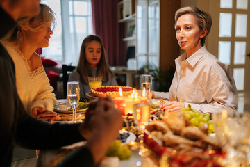 Low-angle view of happy family having xmas party, eating, chatting and smiling sitting at dinner holiday table in dark room with cozy interior on Christmas eve. Concept of home festive atmosphere.