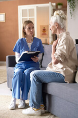 Vertical image of senior woman complaining on her health to doctor while they sitting on sofa in...