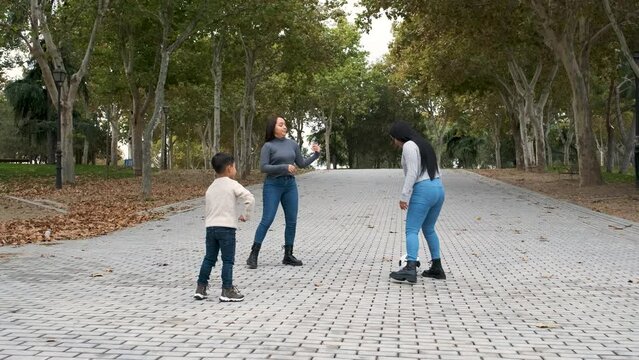 Latin lesbian couple playing football with their son at a park. LGBT family.