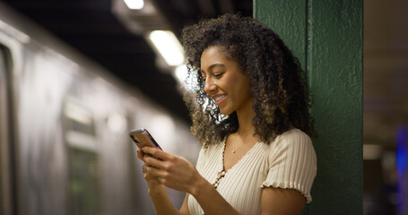Young black woman using smartphone at a subway platform