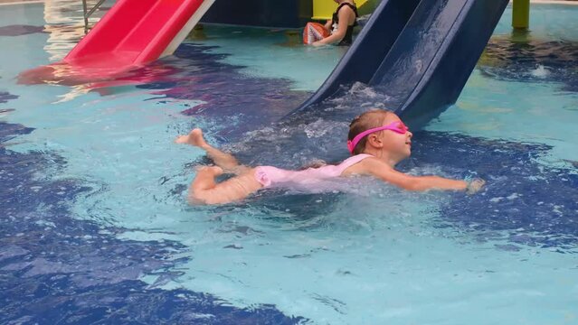 Child sliding into the water in aqua park. Kid having fun and entertaining in indoor swimming pool. Toddler girl making splashes 