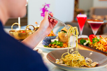 Woman eating pasta on the dining table,Half empty glass of fresh orange juice on table, woman...