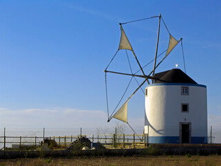 Typical Portuguese windmill from the central and southern regions in Sesimbra, Portugal. View of the cloth sails partially unwrapped from the masts. Backlit silhouette.