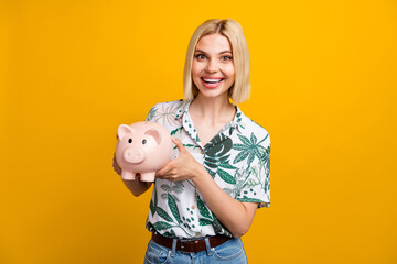 Photo portrait of lovely young lady hold pig money savings wear trendy leaves print garment isolated on yellow color background