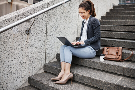 Business woman, stairs and typing on laptop, planning schedule and thinking with ideas, copywriting or city. Young entrepreneur, smile and sitting on steps with computer for remote work in metro cbd