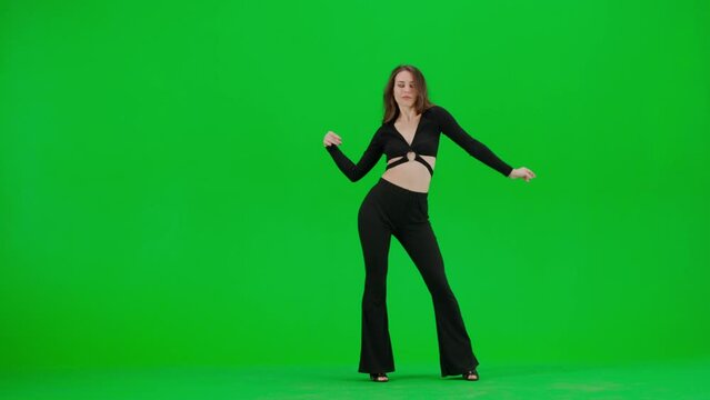 Attractive woman dancing heels dance on green screen chroma key background in a studio. Black sexy costume, high heels. Modern sensual choreography. Full length.