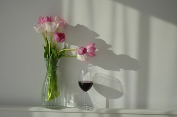 Delicate pink flowers in a vase, with a glass of red wine on the countertop