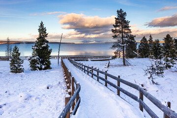 Snow covered walkway in West Thumb Yellowstone National Park Wyoming with clouds and sky reflecting in Yellowstone Lake at sunset.