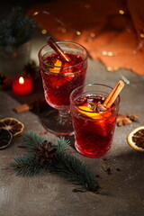 two glasses of mulled red wine with cinnamon and citrus, a fir branch with a cone next to it, Christmas atmosphere, warm brown background