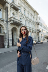 Fashion beautiful sexy woman with a hairstyle in a fashionable blue suit with a trendy bag walks in the city near a vintage building. Successful business lady