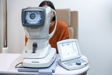 Woman looking through auto refractor machine during an eye examination in a clinic, displaying eye...