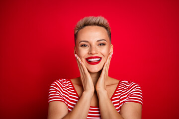 Photo of lovely adorable girl wear stylish clothes two arms touch cheeks showing white teeth visage isolated on red color background