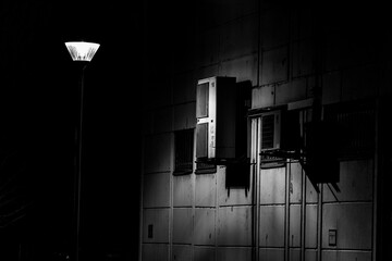 Grayscale of a  lamppost illuminated in the night near a building adorned with closed shutters