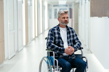Portrait of sad thoughtful grey haired man sitting alone in wheelchair in hospital corridor.