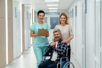 Woman with man in wheelchair talking with female receptionist at clinic.