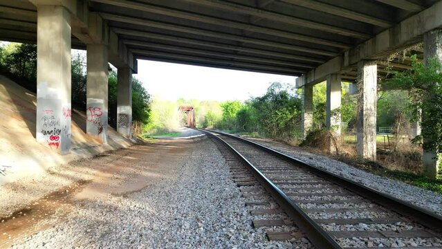 Drone footage of train track passing under bridge with graffiti on pillars near savannah river