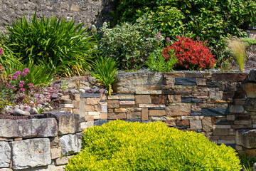 Muret de pierre dans un petit jardin paysagé au printemps. - 672345265
