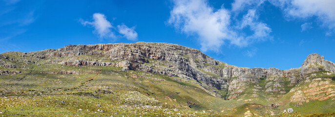 Widescreen landscape view of Table Mountain in Cape Town, South Africa. Low panoramic scenery of a popular natural landmark and tourist attraction during the day against a blue cloudy sky in summer