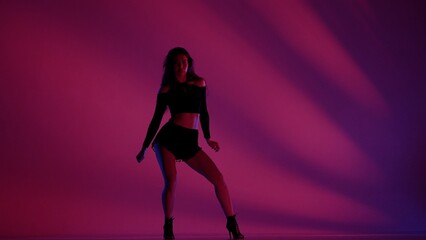 Attractive woman dancing heels dance in a studio. Pink and blue neon lights, striped shadowed background. Black sexy costume, high heels. Modern sensual choreography. Full length.