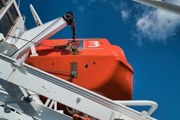 Low angle shot of a lifeboat on the top floor of a ship under a blue sky