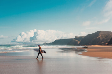 Young female surfer walking into Atlantic Ocean on sandy beach in Portugal