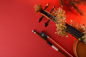 Violin and bow with golden Christmas decoration on red background