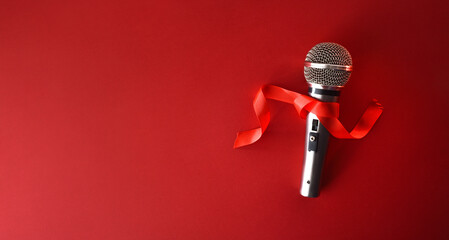 Metal microphone with red bow on red background top view