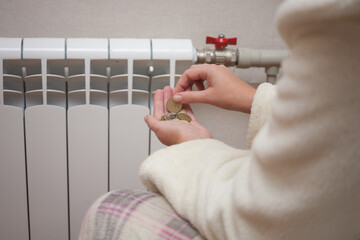 A woman counts coins in her hands near a heating radiator. The concept of paying for heating.