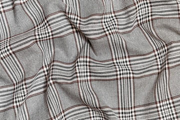 Close-up of crumpled, wrinkled texture fabric of black with brown tartan in check. Material for sewing skirts, shirts and coats. Background for your design