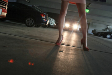 Young woman is afraid in the parking garage. In the background a car with a blinded beam