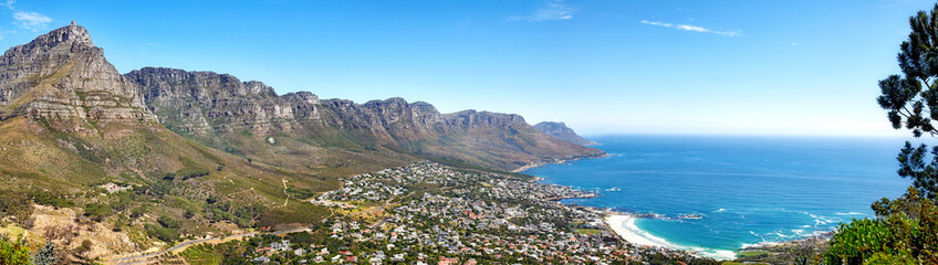 Fototapeta na wymiar Beautiful coastal landscape with mountains surrounded an urban city in a popular tourism destination. Aerial view of Cape Town city with Mountain outcrops and the ocean on a blue sky with copy space