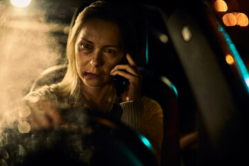 Woman with bruises on face calling someone while driving