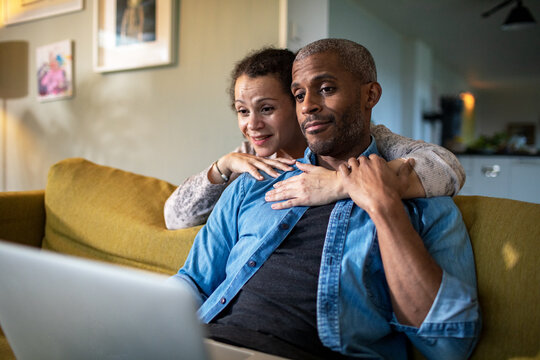 Woman hugging man looking at the laptop together at home