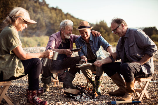 Senior Friends Cooking Fish Over A Fire In Nature