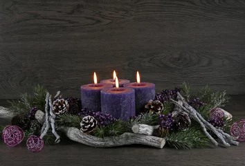 Fotobehang Adventsdekoration: Adventskranz mit vier lila brennenden Kerzen für den vierten Advent mit Tannenzweigen und Weihnachtsdeko vor einer Holzwand mit Platz für Text. © Racamani