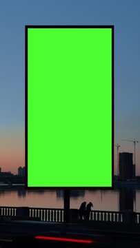 Timelapse under large green billboard on waterfront of night city, reflection of buildings in river, lights of cars passing by. Commercial information and advertising marketing