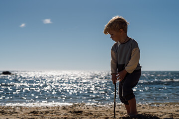 A beautiful three-year-old blond boy walks barefoot on the sandy shore by the sea.