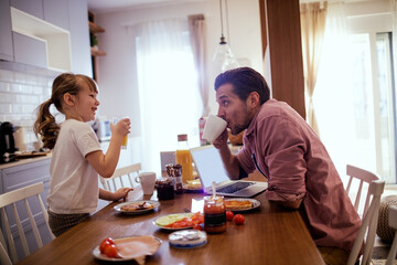 Happy little girl having breakfast with her father in the kitchen