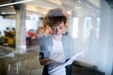 Woman holding a smartphone and document in a office