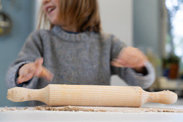 Boy rolling out homemade pizza dough with a rolling pin seen close up