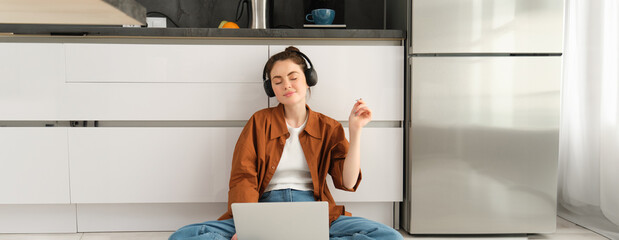 Portrait of young woman, dj mixing sounds on laptop, closes eyes in headphones and listens to...