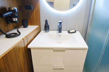 The compact bathroom features a glass shower cabin and a white cabinet. Round illuminated mirror...
