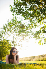 Beutiful dark hair girl with sunglasses lying on a meadow in the park.