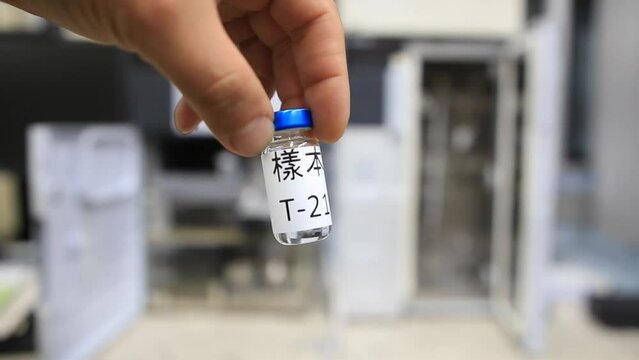 A man holds a vial with a liquid labelled as sample in chinese characters inside a analytical chemistry laboratory