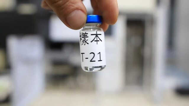 A close up from a man holding a vial with a liquid labelled as sample in chinese characters inside a analytical chemistry laboratory