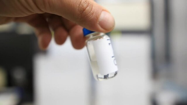 A close up from a man holding a vial with a liquid labelled as sample in hindi inside a analytical chemistry laboratory
