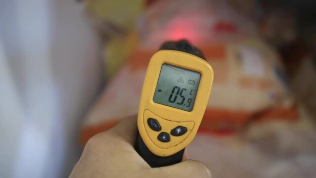 A person uses a infrared thermometer to measure the temperature of food inside a freezer 